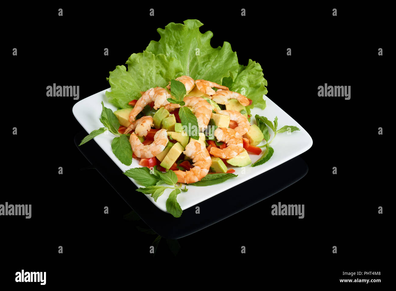 Vietnamese cuisine Avocado salad with shrimps with vegetables on rectangular white plate isolated on black reflective background Stock Photo