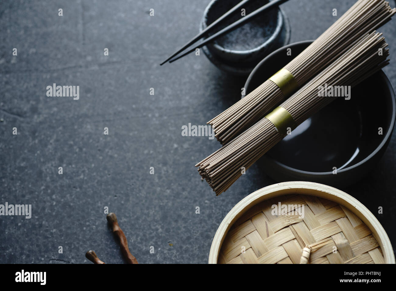 Soba noodles, bamboo steamer and asian cuisine props on dark background with copy space Stock Photo