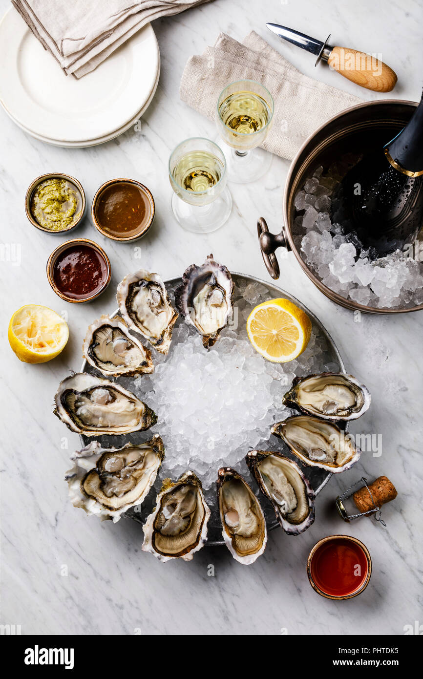 Open Oysters with lemon, sauce and Champagne in ice bucket on white marble background Stock