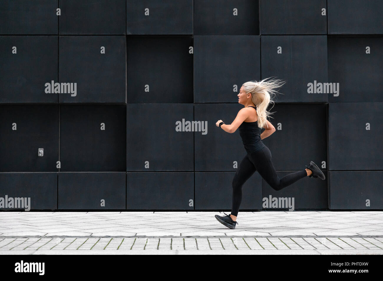 Side view of sporty young woman running fast in minimalist urban environment Stock Photo