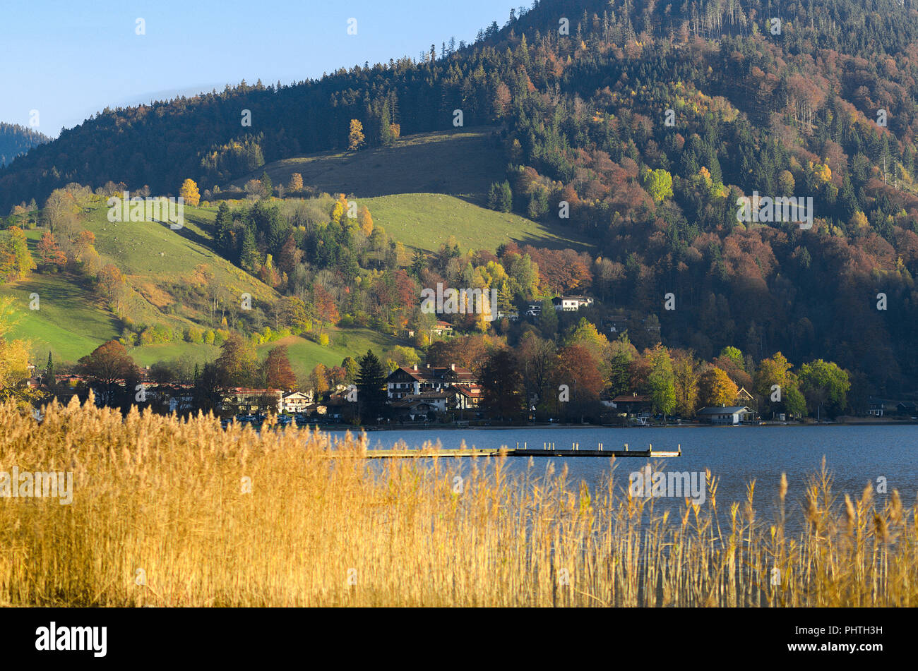 Autumn landscape with township in Upper Bavaria near mountain lake with pier and dry reed Stock Photo
