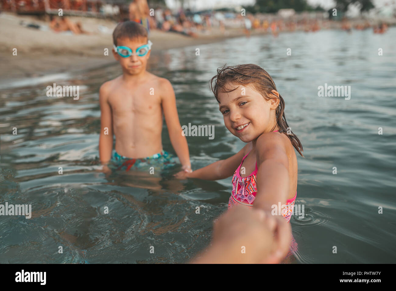 Happy children playing in the sea. Kids holding hands and invite their  mother to go with them. Summer vacation and healthy lifestyle concept Stock Photo