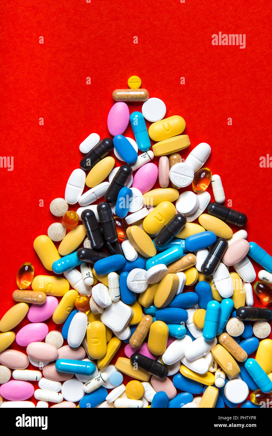Piled up mountain of colourful pills, medication against red background Stock Photo