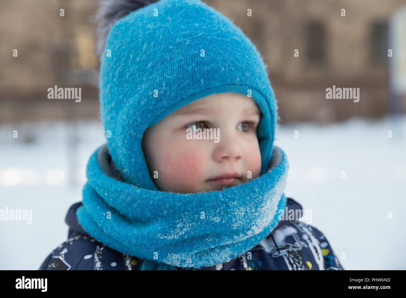 Child boy 2-3 years in winter outside in blue knitted woollen hat with pompon and scarf-snood. Close-up portrait Stock Photo