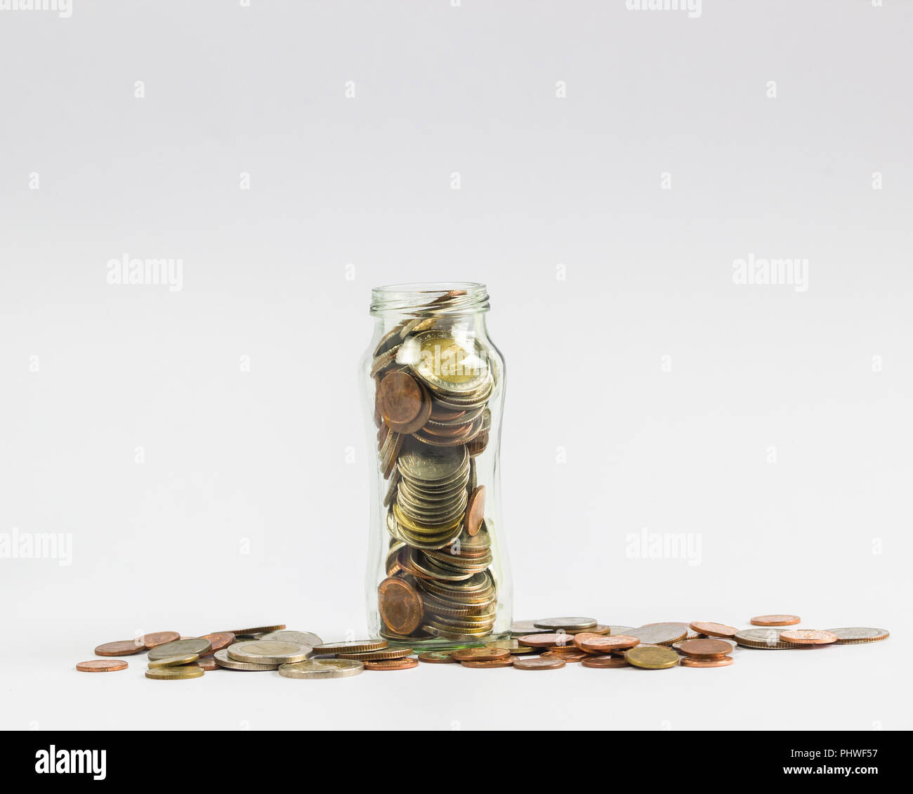 Savings, Investment growing money concept : A full coins in a clear glass jar with many coin on white background. Stock Photo