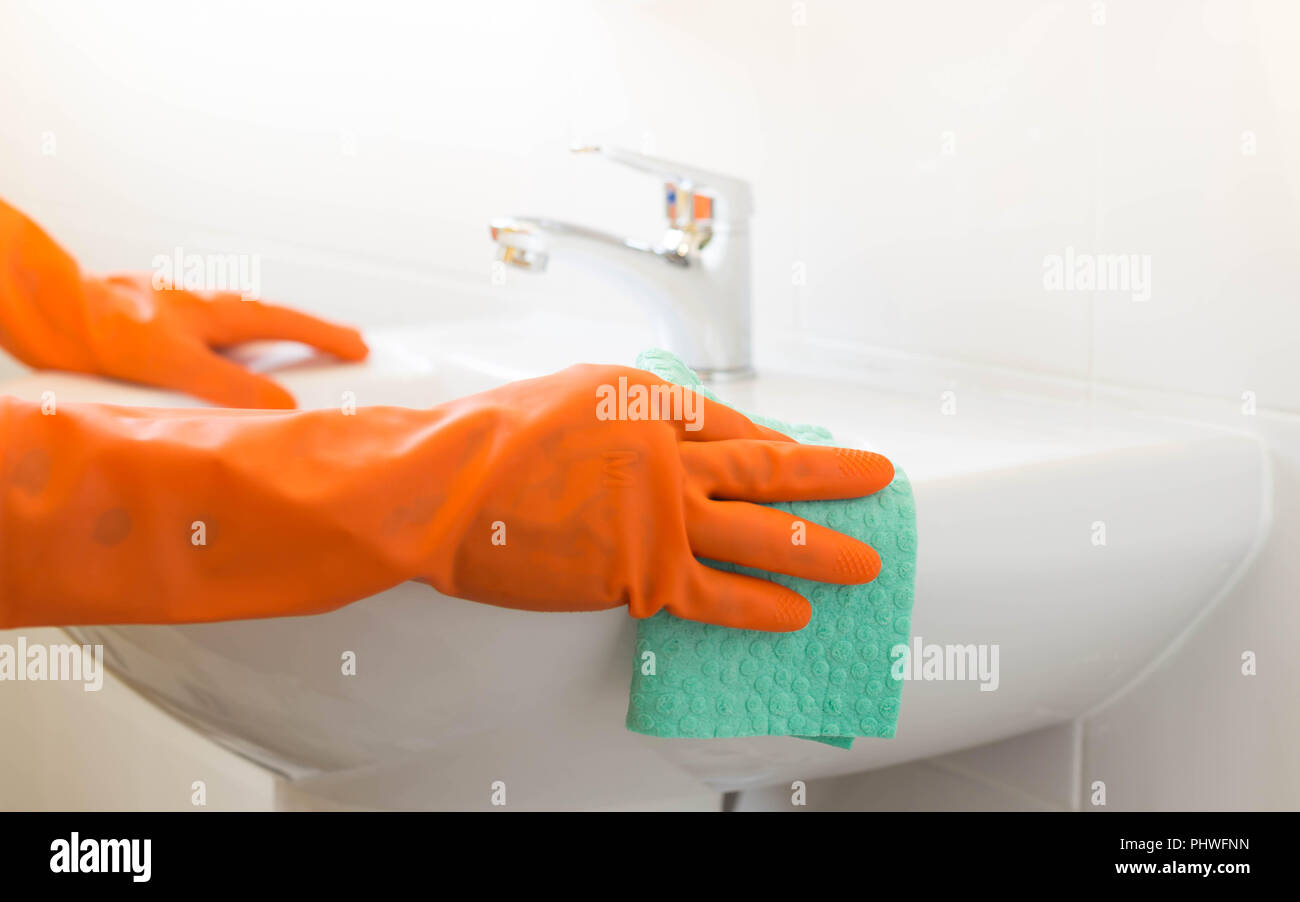 Woman cleaning water tap witn orange glove Stock Photo