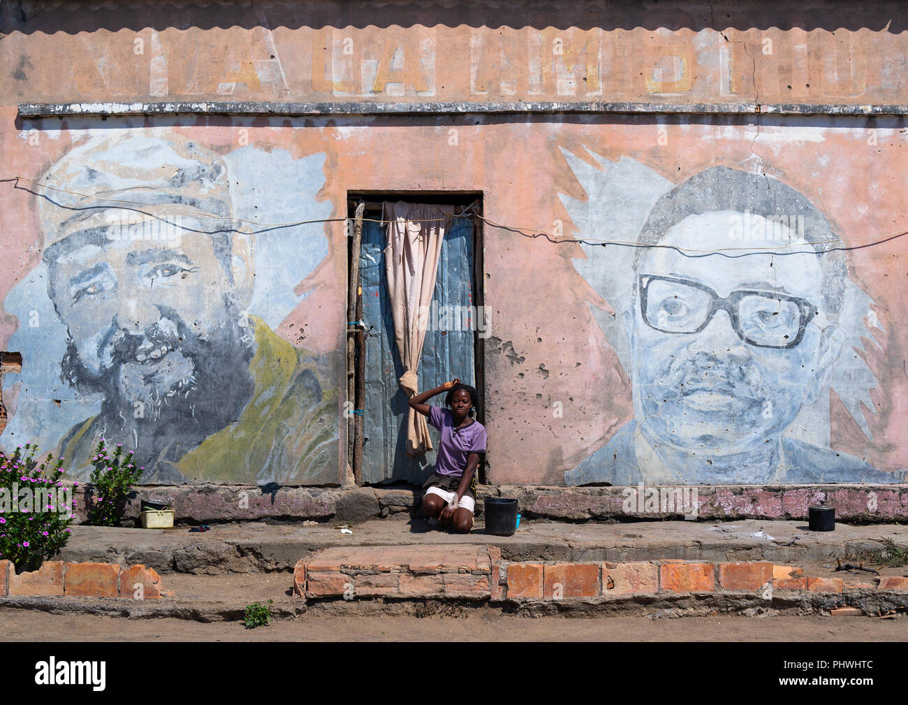 Woman in front of an old propaganda wall painting with Fidel Castro and Jose Eduardo dos Santos, Cunene Province, Cahama, Angola Stock Photo