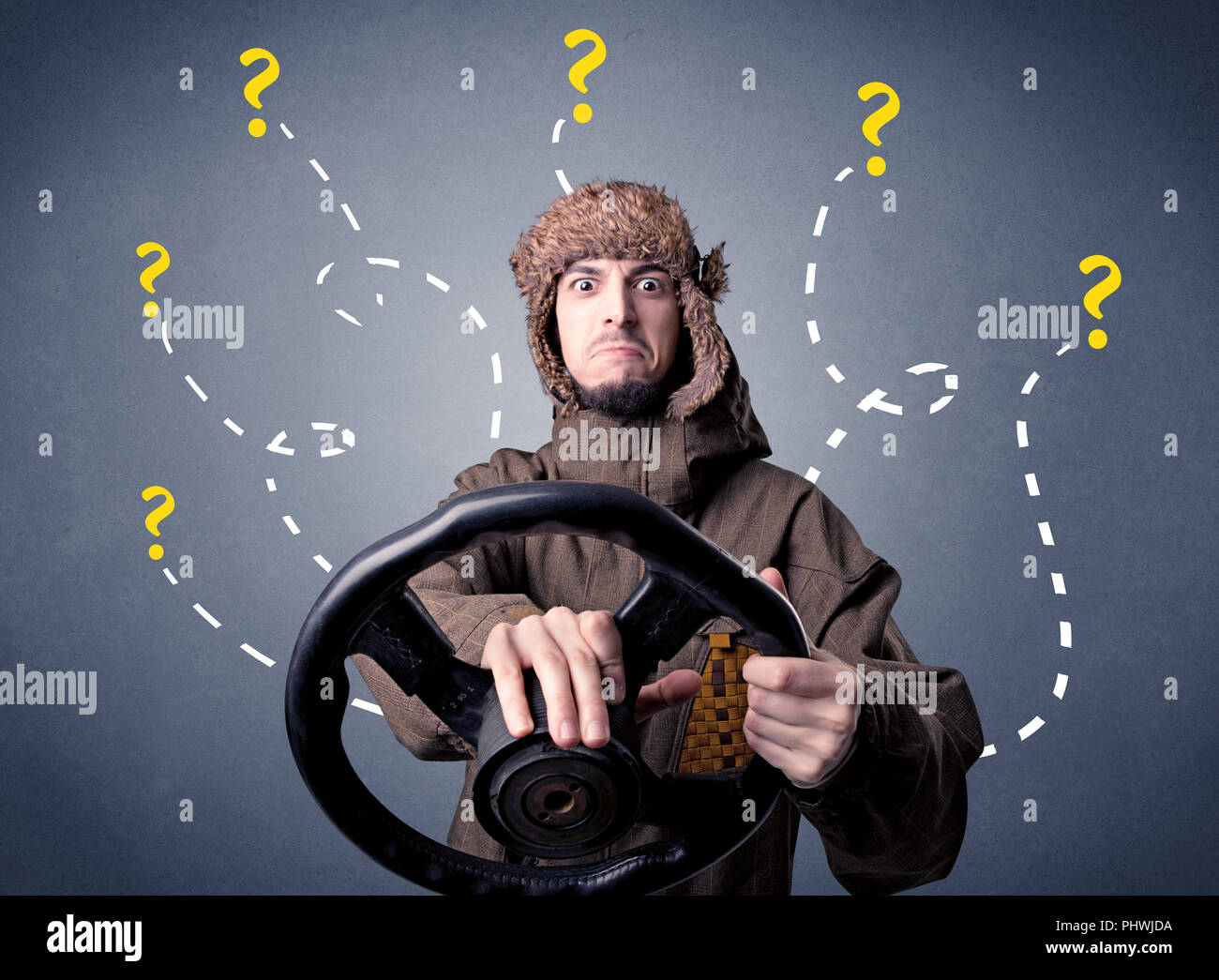 Young man holding black steering wheel with question marks around him