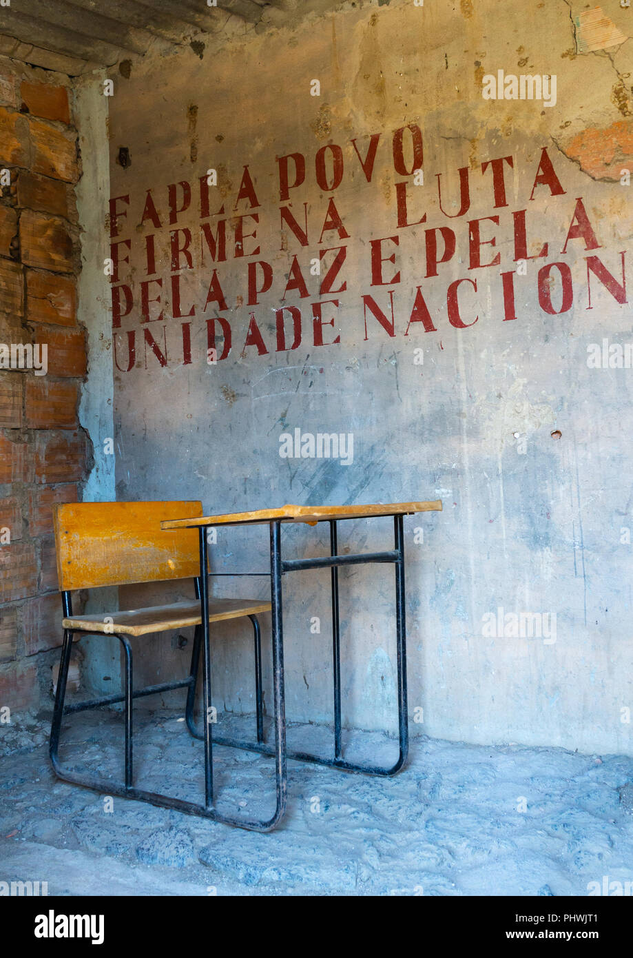 School desk in a classroom with old propaganda on the wall about forcas armadas populares de libertacao de angola popular armed, Cunene Province, Caha Stock Photo