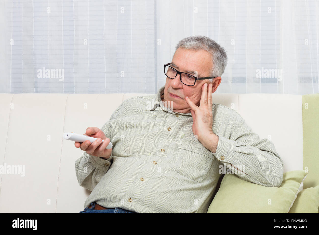 Senior man is trying to find something interesting on tv to pay his attention,but there is nothing interesting. Stock Photo
