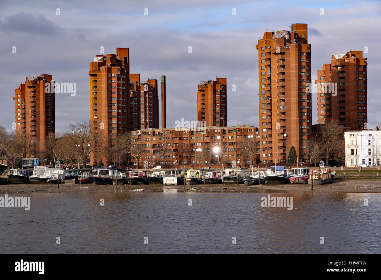 High rise World’s End estate in Kensington and Chelsea, in bold red brick, seen with houseboats moored on the foreshore of the River Thames Stock Photo
