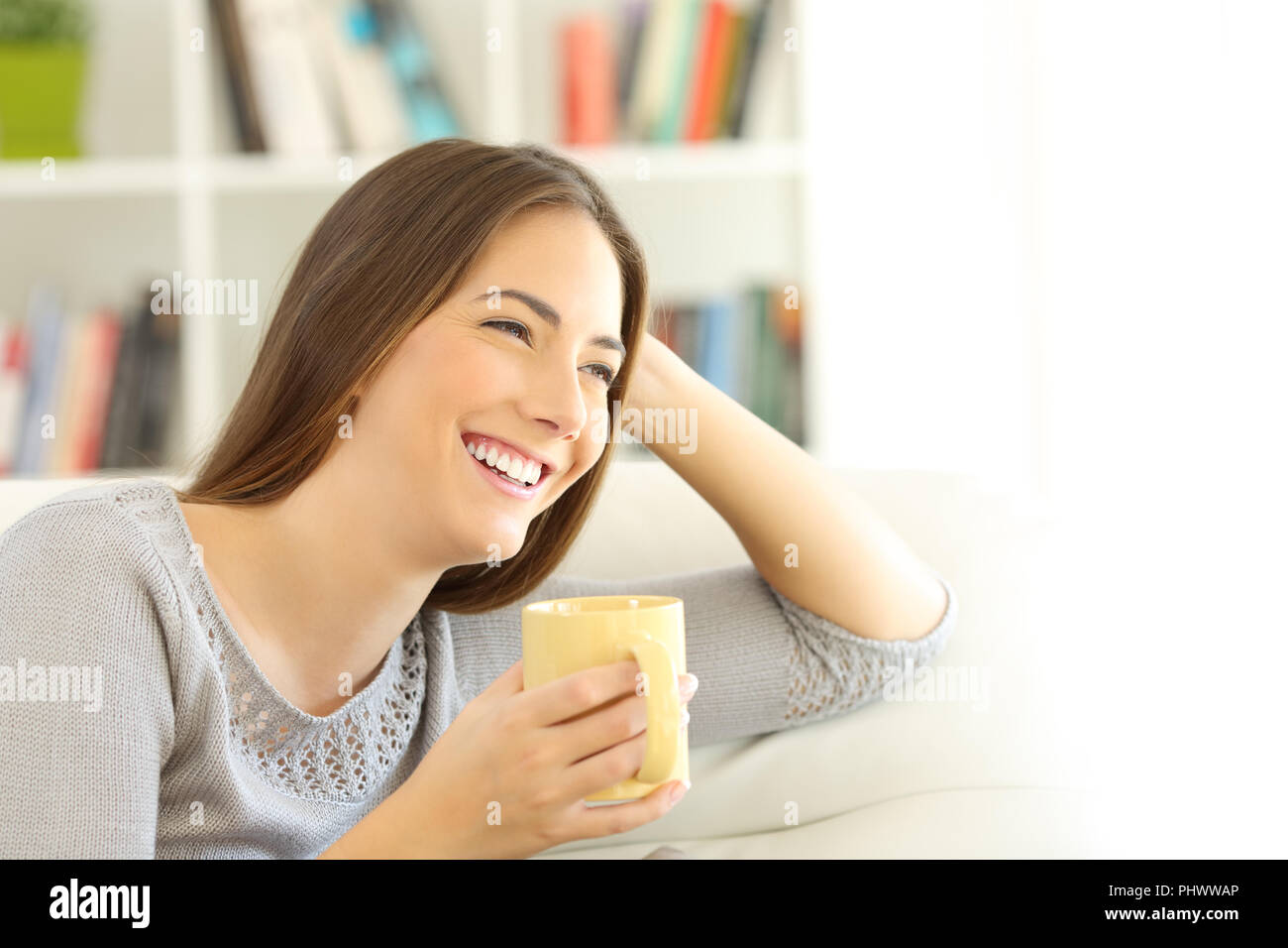 Happy woman thinking looking at side sitting on a couch in the living room at home with white isolated space at side Stock Photo