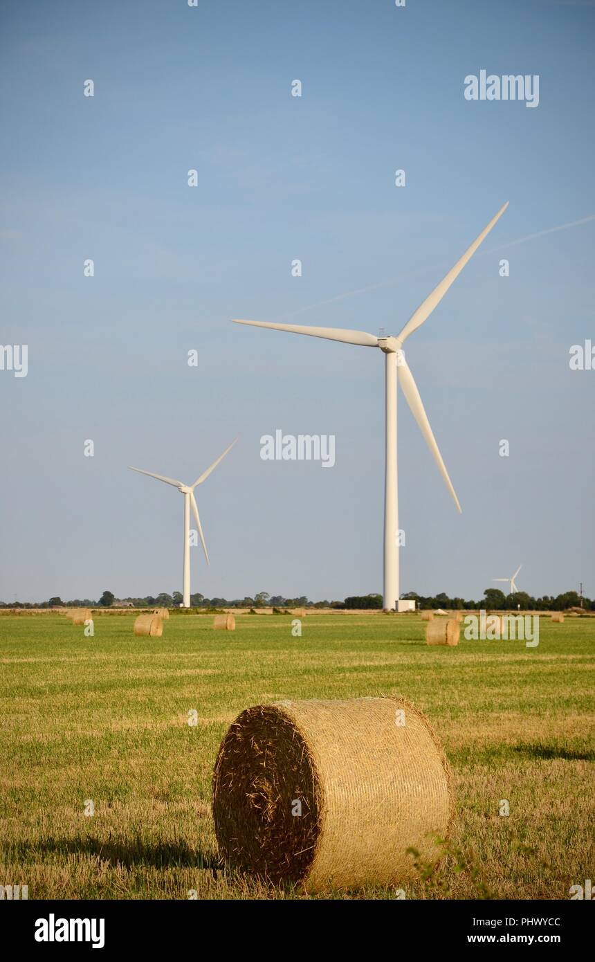 Wind turbines on farm land with round straw bales against blue sky Gayton le Marsh, Lincolnshire, UK Stock Photo