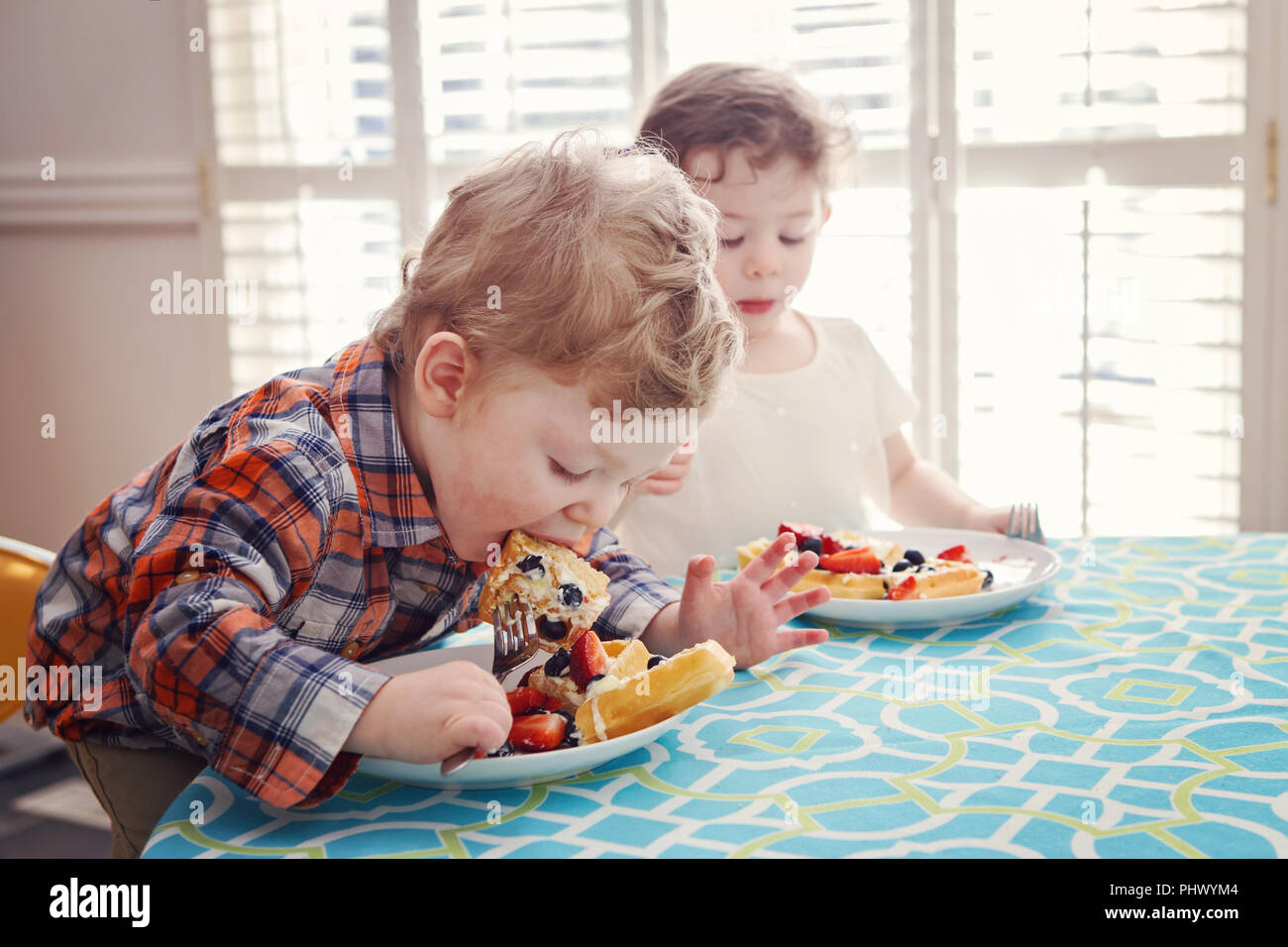 Two happy kids twins boy girl eating breakfast waffles with fruits