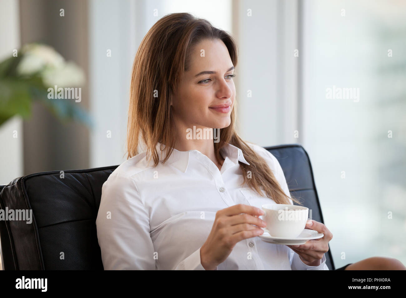 Successful happy woman sitting in chair looking away drinking co Stock Photo
