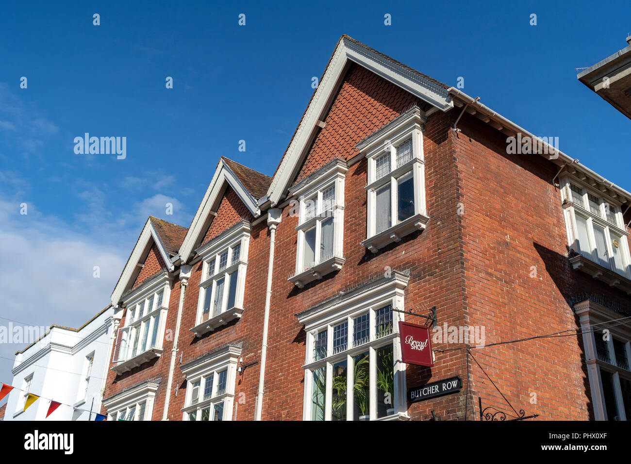 Tall red brick building with three pitched roofs and windows with blue sky above Stock Photo