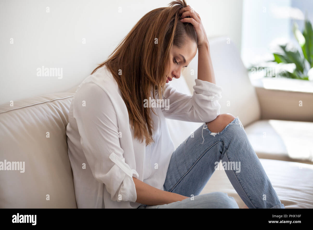 Sad depressed woman feeling bad at home sitting on sofa Stock Photo