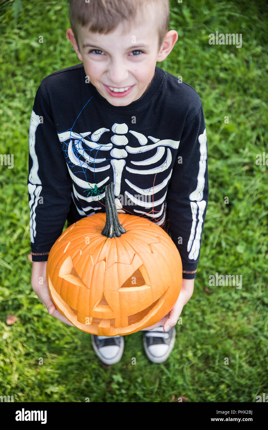 Boy in skeleton costume holding pupmkin at halloween Stock Photo