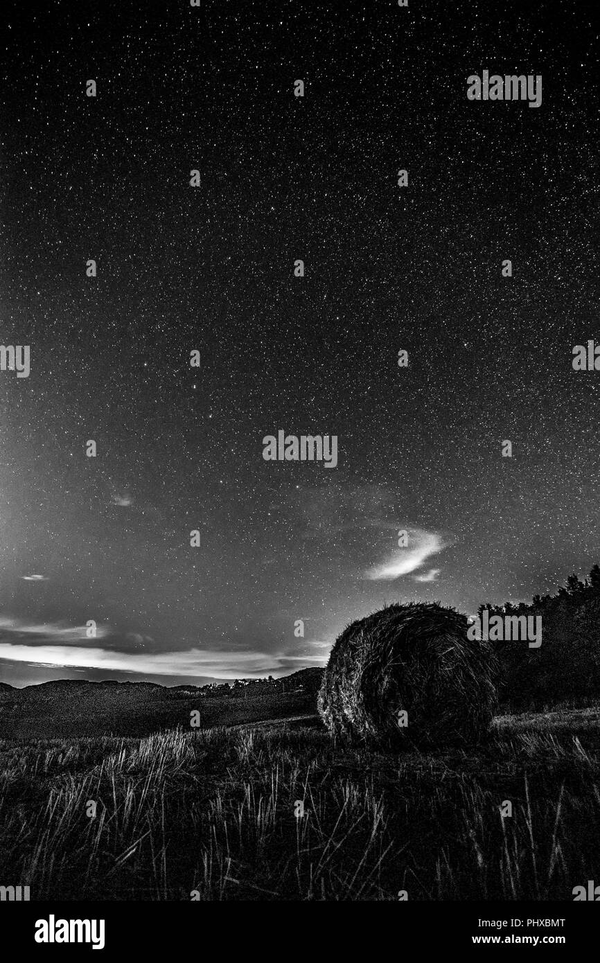 Beautiful view of starred night sky with clouds over a cultivated field with hay bale Stock Photo
