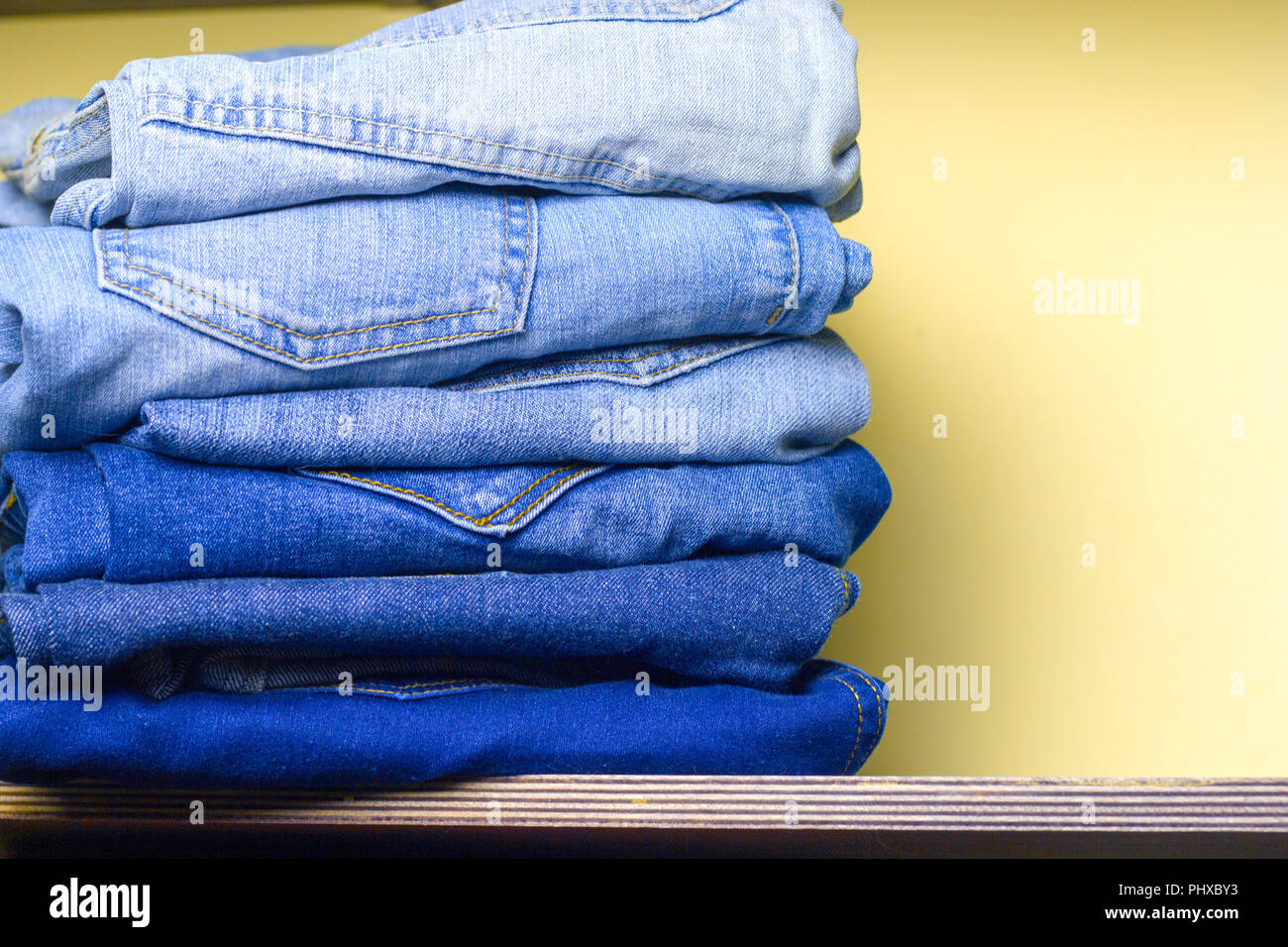 stack  of blue  jeans on a wooden  shelf yellow wall for background Stock Photo