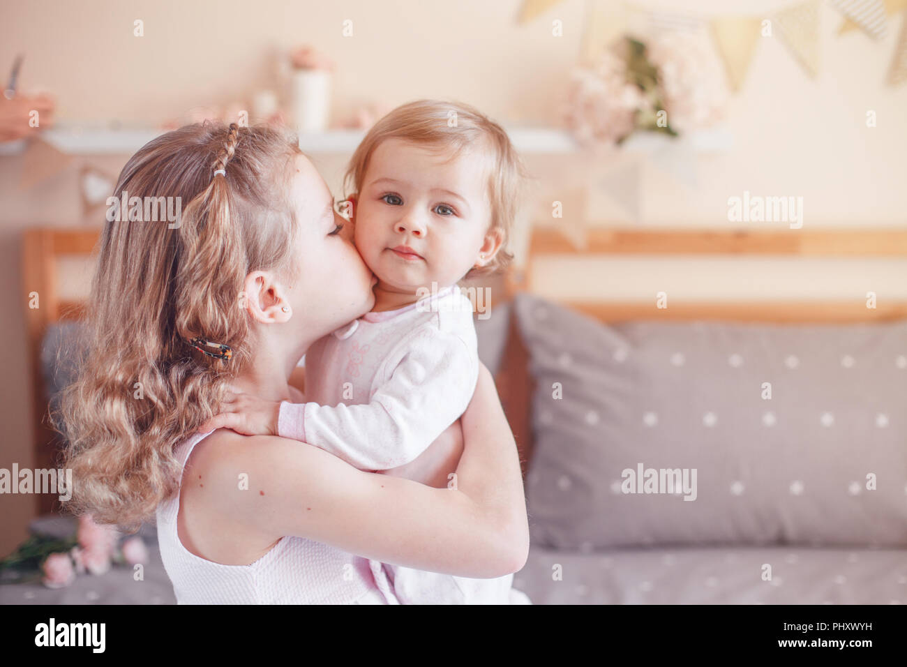 Two cute adorable white Caucasian girsl sisters kissing. Children sitting together on bed in bedroom playing. Lifestyle real true emotions, sibling lo Stock Photo