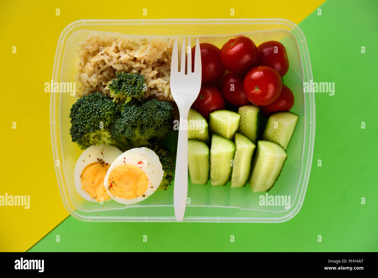 Lunch box with healthy food. Rice, broccoli, tomato, cucumber, eggs, apple and water. On yellow and green background Stock Photo