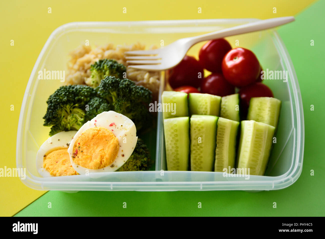 Lunch box with healthy food. Rice, broccoli, tomato, cucumber, eggs, apple and water. On yellow and green background Stock Photo