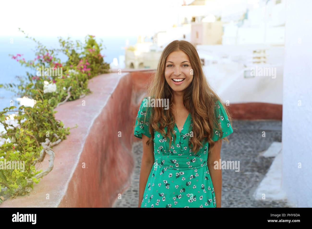 Santorini travel tourist woman visiting famous white village of Oia. Smiling tanned girl in green dress climbs the stairs in Santorini, Cyclades, Gree Stock Photo