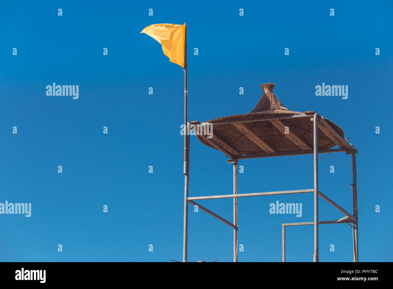 A yellow flag flies from a tall lifeguard tower on the sea. Stock Photo