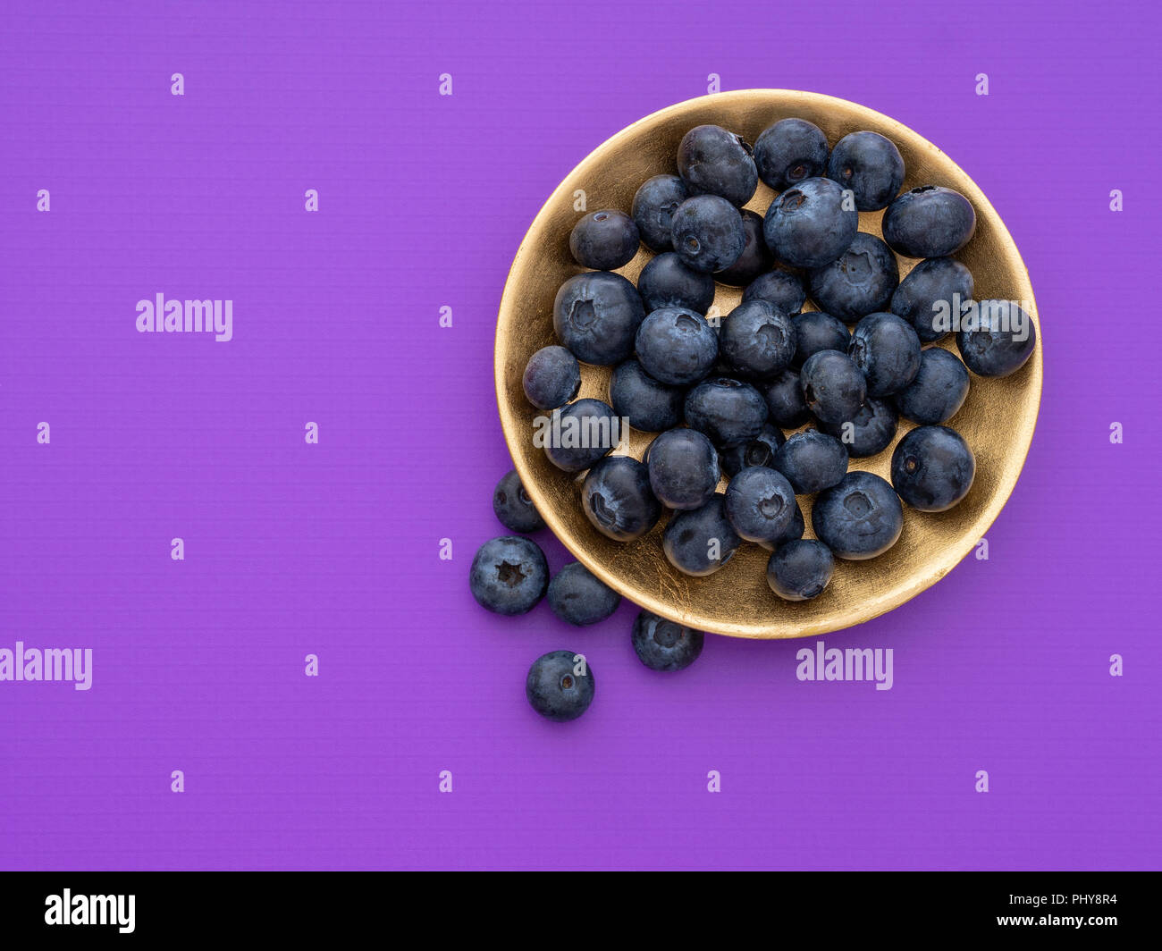 Beautiful healthy superfood blueberries on beautiful gold coloured plate on purple, violet with copyspace. Stock Photo