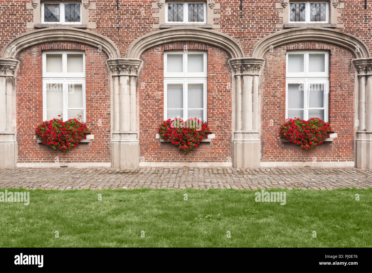 Three medieval archways and a brick façade with red flower bushes in the shape of hearts. Stock Photo