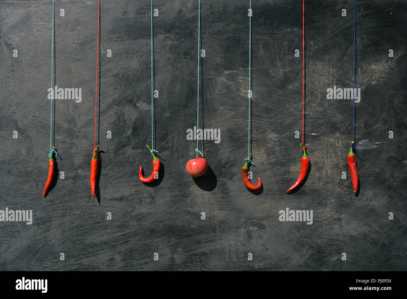 Hanging on colorful strings group red hot chili peppers and apple on old wooden background Stock Photo