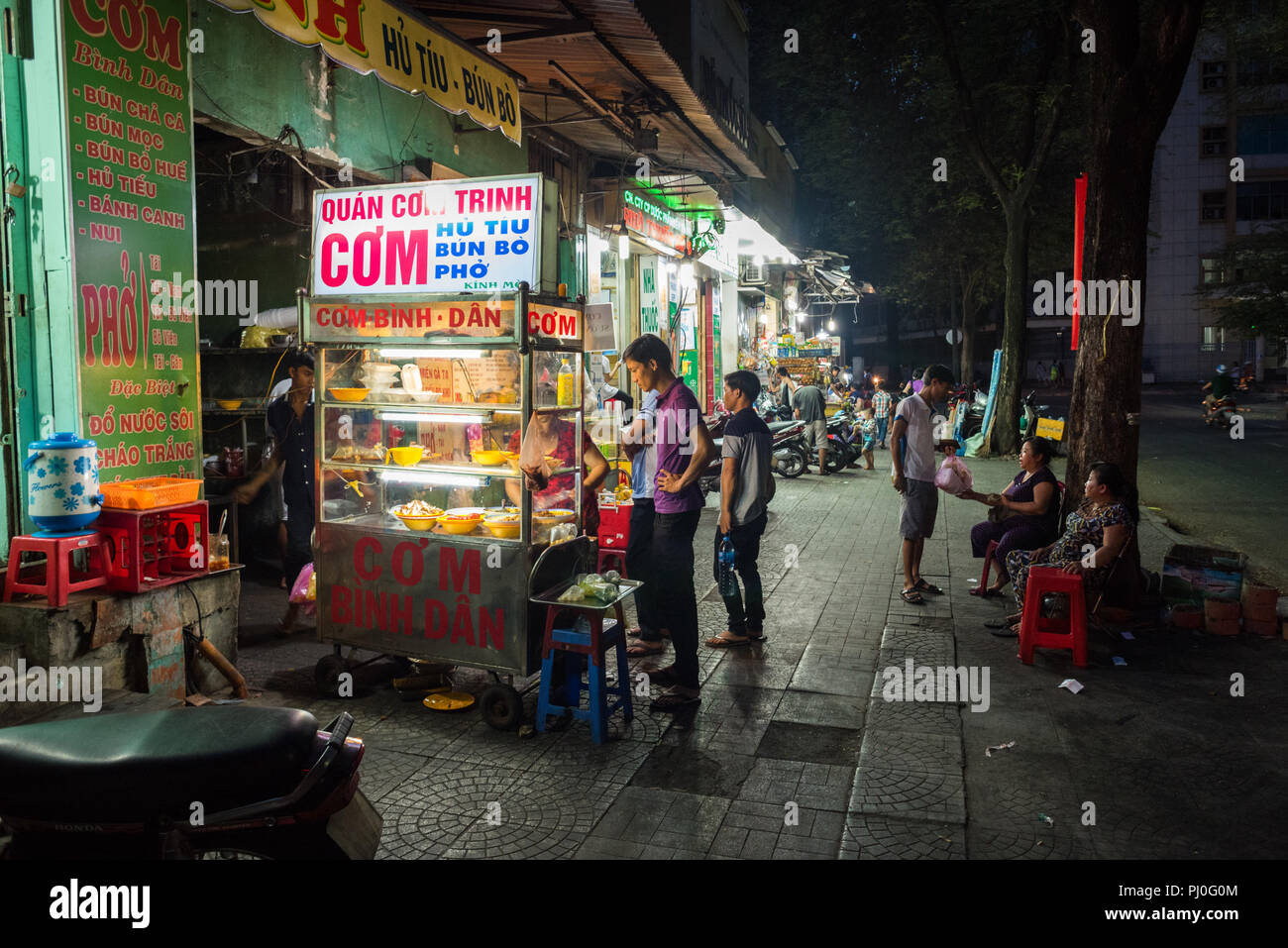 Ho Chi Minh City, Vietnam - May 1, 2018: street food vendors serve a man near the cart in the night street. Stock Photo