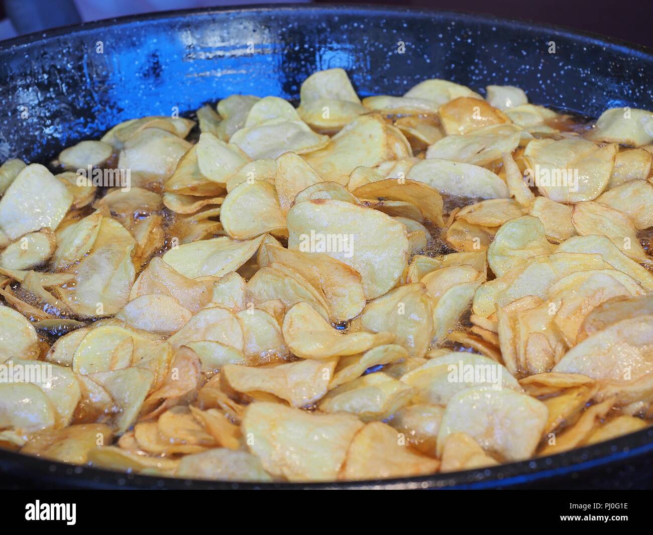 Frying chips in a black pan with a lot of boiling oil in a restaurant