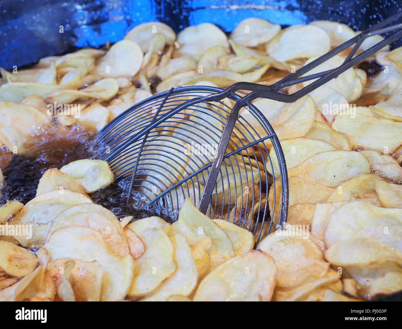 Frying chips in a black pan with a lot of boiling oil in a restaurant