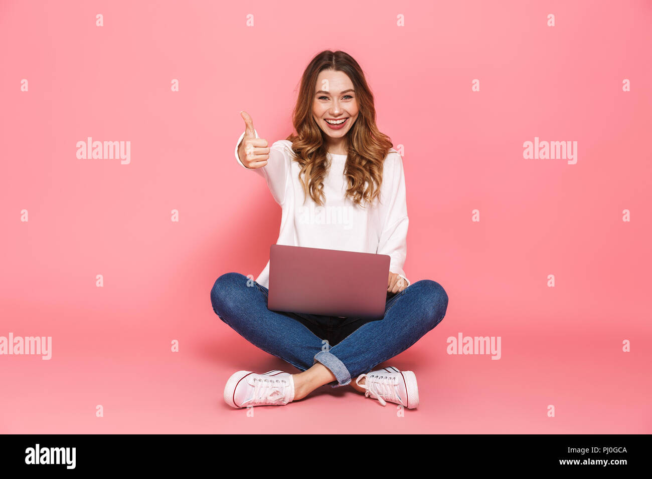 Portrait of a happy young woman sitting with legs crossed, using laptop ...