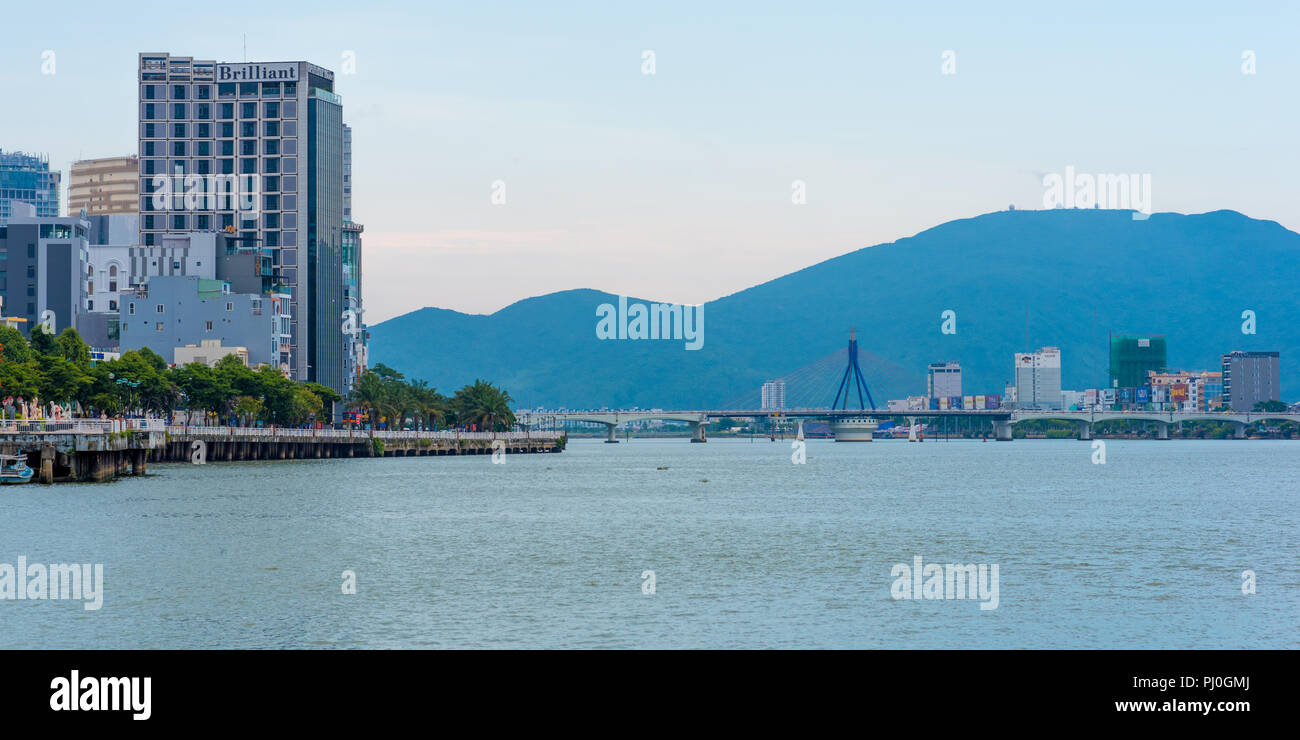 Da Nang, Vietnam - May 6, 2018: The Han River, Song Han Bridge with mountains, the embankment (Bach Dang Street) & 4-star Brilliant Hotel in evening. Stock Photo