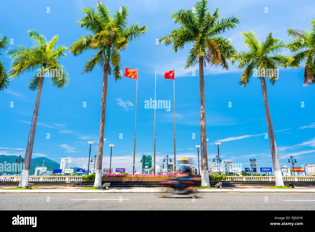 This is Vietnam: palm trees, azure sky, frantic motorbikes and red flags. Stock Photo