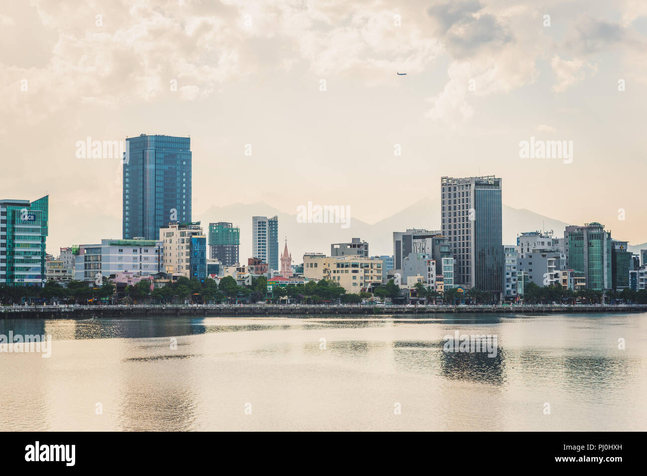 Da Nang, Vietnam - May 7, 2018: the central part of the city (with Danang Cathedral), the Han River, an airplane in the sky & silhouette of mountains. Stock Photo