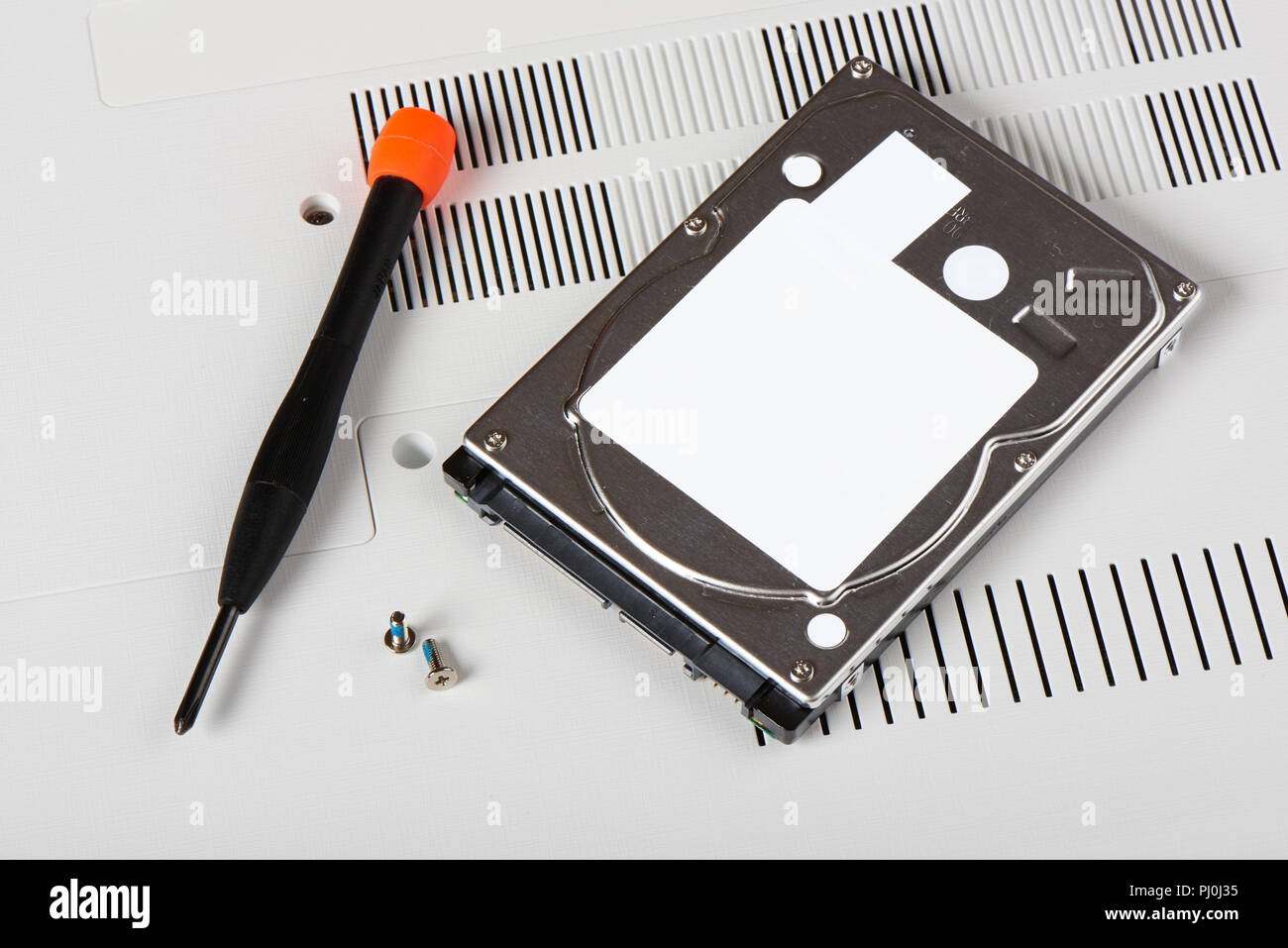 HDD(Hard Disk Driver) with screws and screwdriver on a bottom of laptop Stock Photo