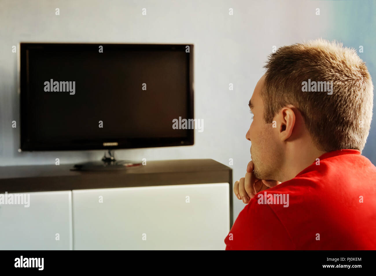 The young guy watches the TV turned off carefully. Single man on the couch watching tv, changing channels Stock Photo