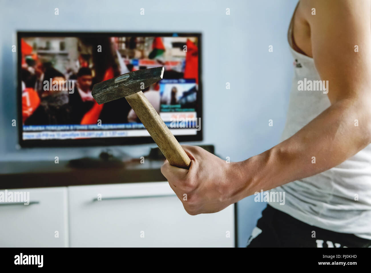 man watches TV news report about the protests. angry guy smashes TV with hammer. false news caused anger among viewers. explosive nature. An angry vie Stock Photo