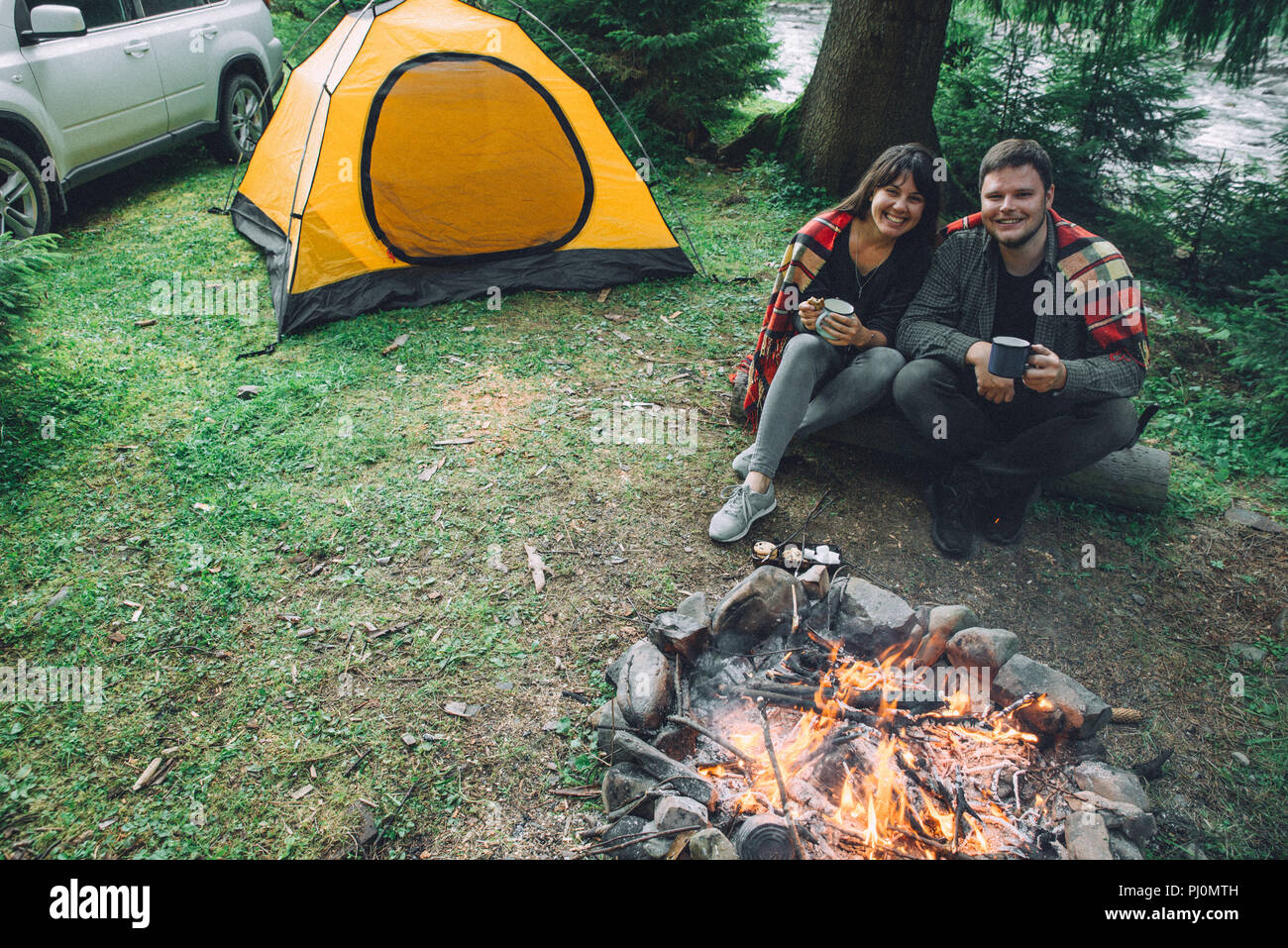 couple sitting near camp fire and drinking tea and telling stories . tent  and suv on background. union with nature Stock Photo - Alamy