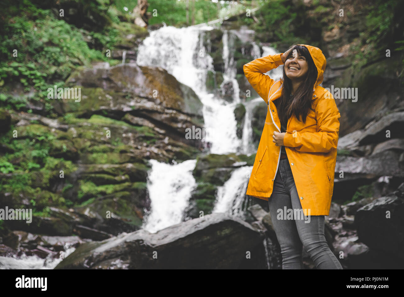 woman standing in yellow raincoat and looking at waterfall. hiking ...