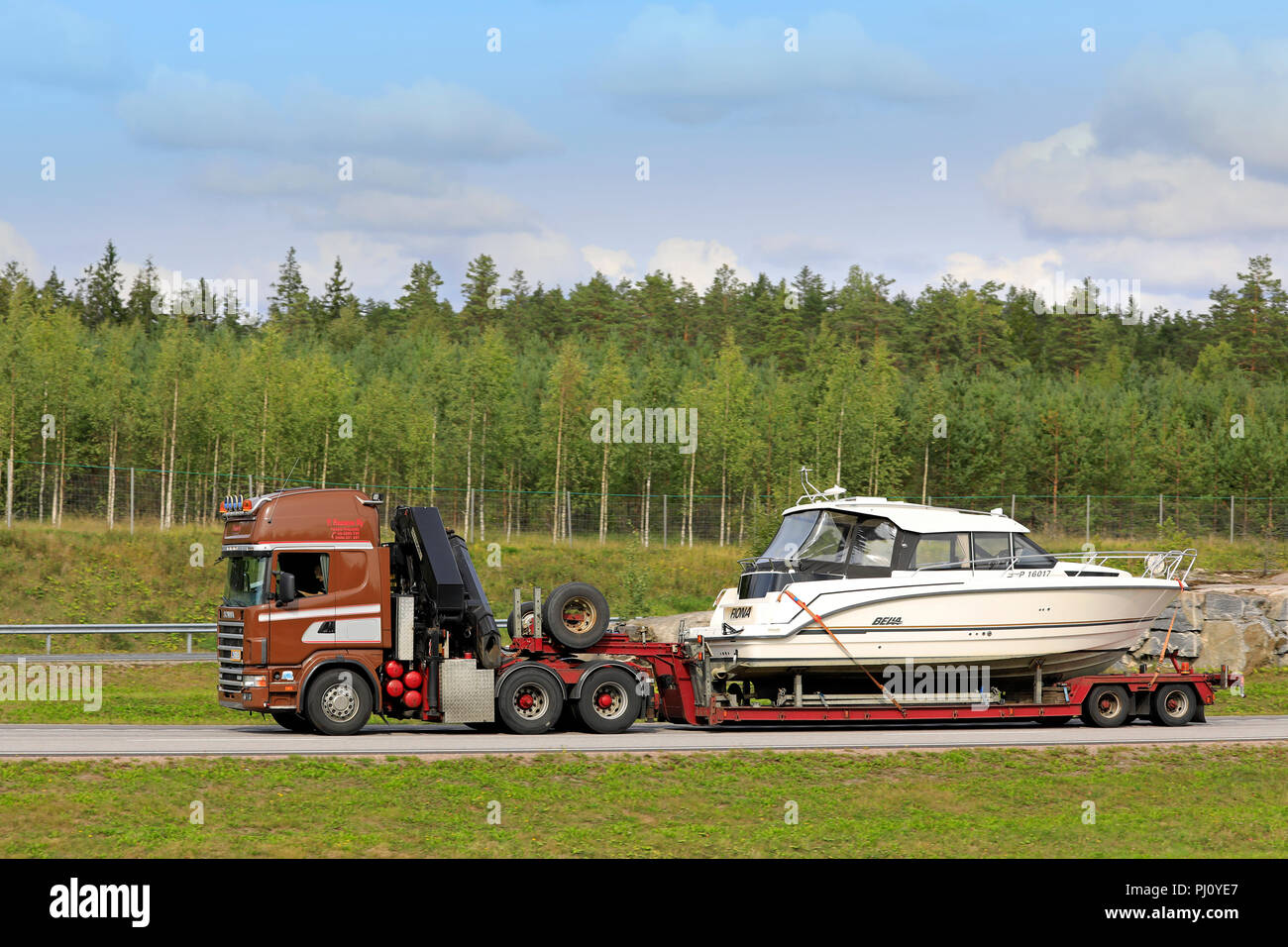 Brown Scania 144 semi trailer of P Husonen Ky transports recreational boat on freeway in late summer in Paimio, Finland - August 31, 2018. Stock Photo