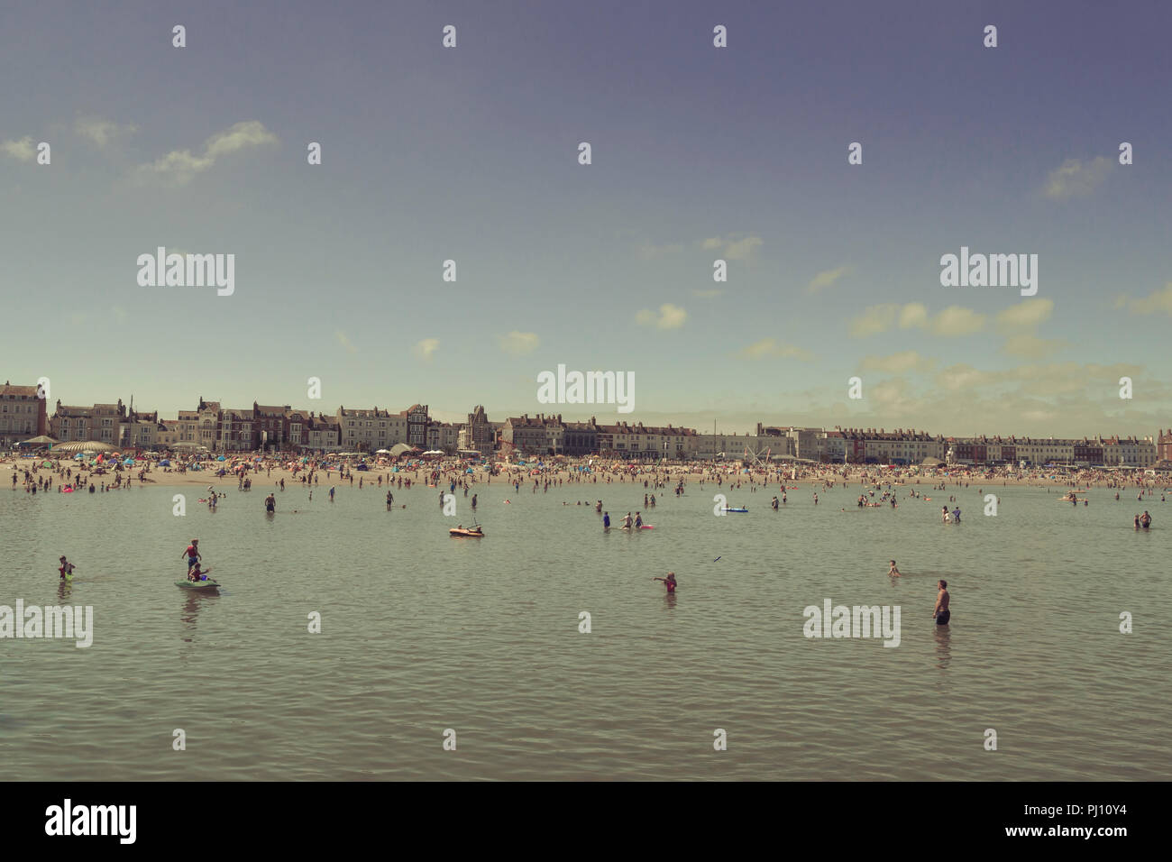 People enjoying the warm weather and shallow waters by Weymouth beach