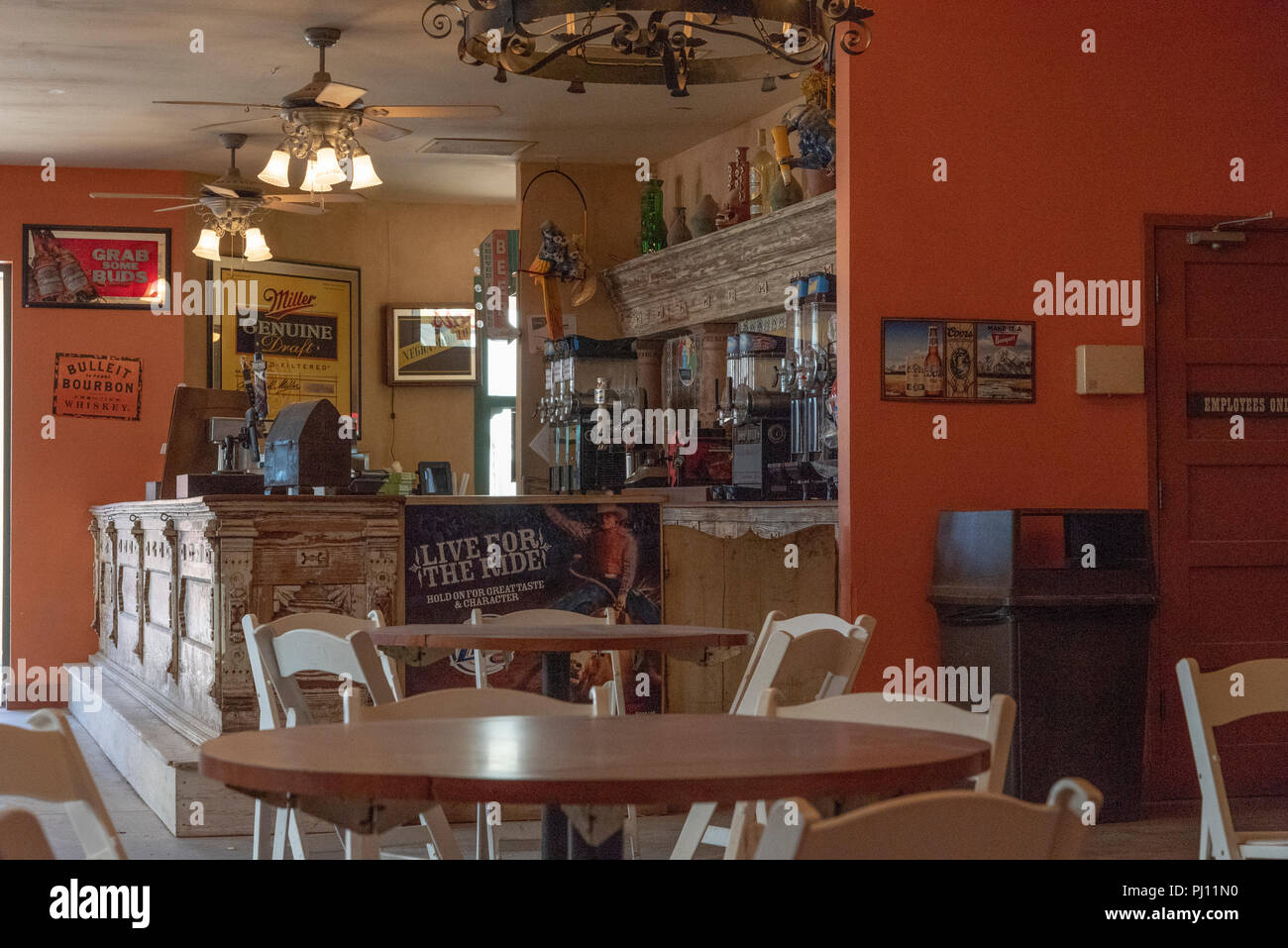 Interior of restaurant bar, round tables and folding chairs.  Wall displays pictures and posters of western movies. Stock Photo