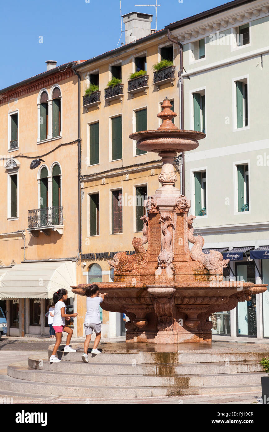 Two little girls playing in the historic  fountain, Piazza Garibaldi, Bassano del Grappa, Vicenza, Italy in the early morning on a hot summer day Stock Photo