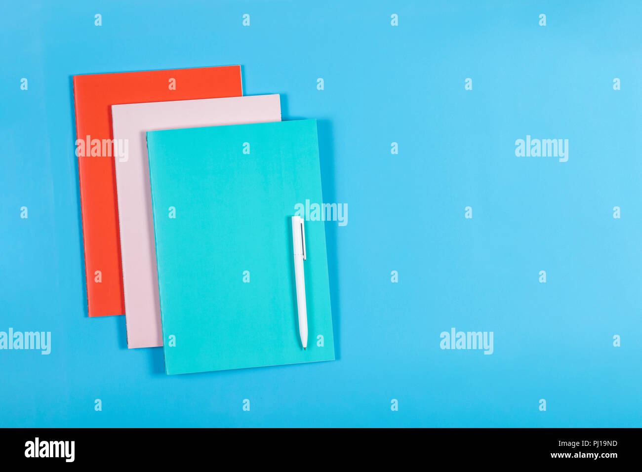 Colorful notebooks and white pen on blue background Stock Photo
