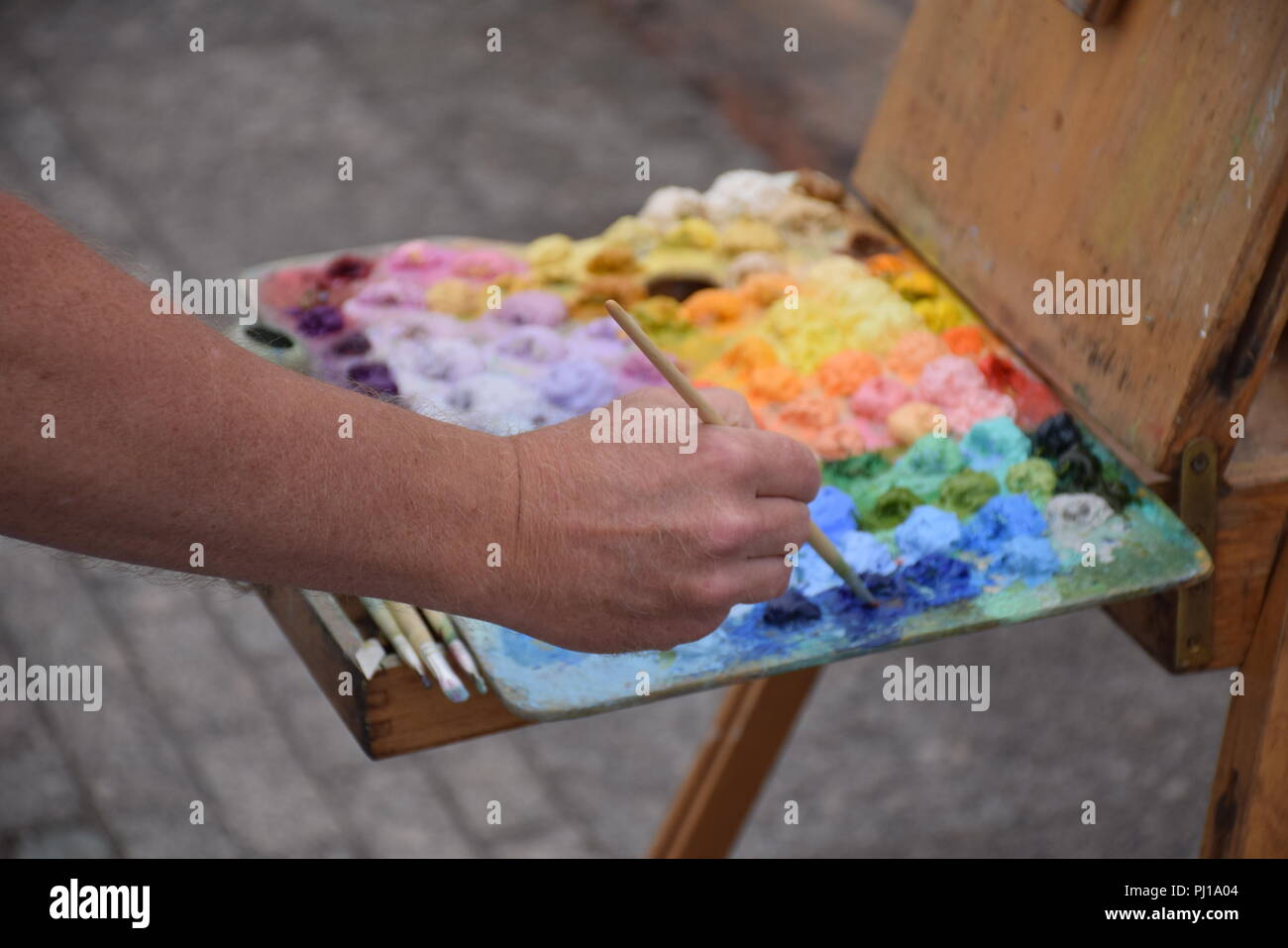 Close up of a hand holding a brush and mixing colors on a color palette Stock Photo